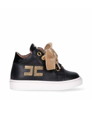 Sneaker in pelle nera con suola bianca, occhielli dorati e un grande fiocco in velluto beige. Presenta un logo decorativo con borchie dorate.