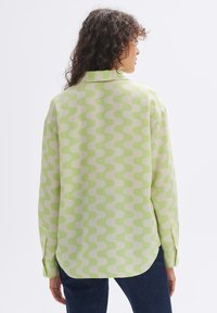 Long-sleeve shirt in light green and cream with a wavy pattern. Soft fabric, collared design, and relaxed fit with rounded hem.
