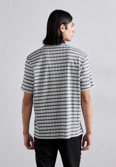 Chemise à manches courtes en motif à carreaux noir et blanc, avec une coupe droite et une texture de tissu lisse. La vue arrière montre l'encolure et l'ourlet.