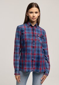 Niebieska i czerwona koszula w kratę z długim rękawem, wykonana z miękkiego materiału. Posiada zapięcie na guziki, kołnierz oraz kieszeń na lewej piersi.
