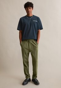 T-shirt en coton bleu foncé avec impression "EARLY BIRDS" ; pantalon fuselé vert olive avec taille à cordon et bandes latérales ; chaussures noires.