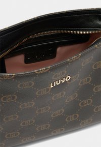 Zwarte gestructureerde leren tas met een bruin patroon logo ontwerp. Gouden hardware details en een roze stoffen interieur met een ritsvak.