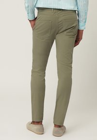 Green cotton chinos with a slim fit, featuring two back pockets and a smooth texture; paired with light-colored shoes.