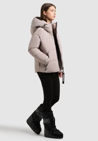 Gevoerde lichtgrijze winterjas met een grote capuchon, vooraan ritsen en zijzakken, gecombineerd met zwarte gestructureerde sneeuwlaarzen.