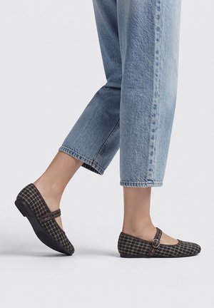 Pies con zapatos planos Mary Jane a cuadros marrones y negros con hebilla, combinados con vaqueros cropped azul claro.