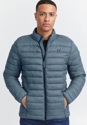 Chaqueta inflable azul con patrones acolchados horizontales, cuello alzado, cremallera frontal y bolsillos laterales, confeccionada en un material ligero y suave.