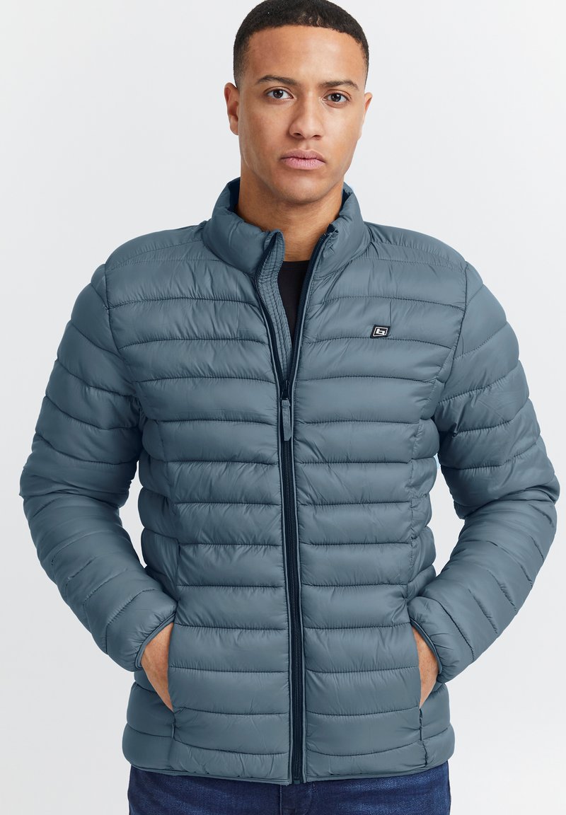 Giacca puffa blu con motivi a rombi orizzontali, collo alto, cerniera frontale e tasche laterali, realizzata in un materiale leggero e liscio.