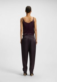 Satijnen bordeaux camisole met kant, gecombineerd met losse, donkere broek met een gladde textuur en achterzakken. Zwarte hakken.