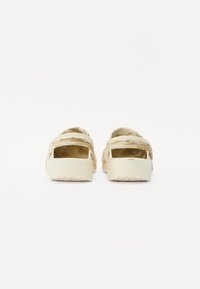 Light beige clogs with an open back, textured rubber material, adjustable straps, and ridged soles for grip.