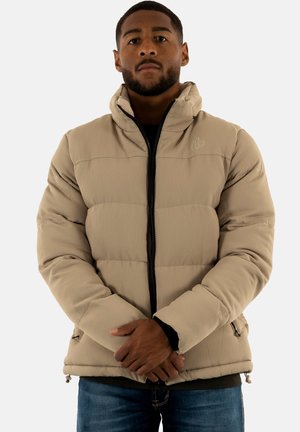 Giacca a vento beige con texture a coste, zip frontale, colletto alto e tasche laterali. Indossata sopra un top scuro, con una vestibilità comoda.