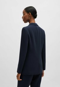 Marinblå skräddarsydd kavaj av mjukt tyg, med slagkrage och långa ärmar, med en slank, minimalistisk design och detalj vid bakseam.