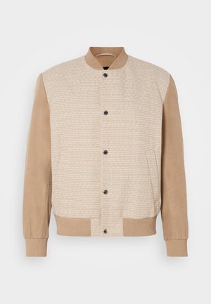 Veste bomber tan avec un devant en tissu texturé et des manches en daim lisse. Présente un col et un ourlet côtelés, ainsi que cinq boutons sur le devant.