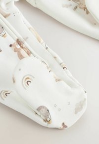 Ensemble de bébé en coton blanc avec des motifs d'animaux marron clair, des arcs-en-ciel et de petites étoiles. Texture douce avec une fermeture éclair et des pieds enfermés.