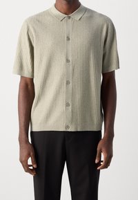Korte mouwen, geribbeld gebreid poloshirt in lichtgroen met een opgebouwde kraag en vijf knopen, met een relaxte pasvorm en een zachte textuur.