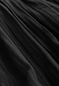 Tissu noir avec des plis verticaux doux et irréguliers créant des plis texturés, fluides et des ombres.