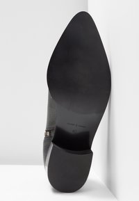 Grauer Lederschuh mit spitzem Zeh und glatter schwarzer Sohle. Eigenschaften sind ein strukturiertes Obermaterial und eine metallische Akzentuation nahe dem Knöchelriemen. Größe 40.