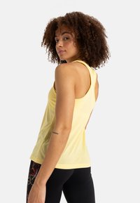 Gelbes ärmelloses Tanktop aus weichem Stoff, mit einem Rundhalsausschnitt und einem Racerback-Design. Getragen mit schwarzen Leggings.