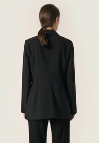 Must tumed blazer, mille struktuurse disainiga, lõigatud krae ja sirge lõikega. Omab sujuvat tekstuuri ja minimaalset kaunistust.