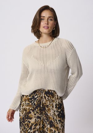 Maglione a maglia beige chiaro con ampia trama a rete, scollo rotondo e maniche lunghe, abbinato a pantaloni larghi con stampa leopardata.