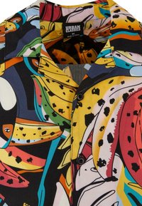 Chemise à manches courtes avec un motif coloré de banane et abstrait. Fabriquée en tissu léger, elle présente un col cranté et un bouton noir.