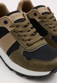 Zapatillas de hombre en negro, caqui y beige. Presentan texturas de malla y gamuza, puntera redonda, cordones gruesos y una entresuela blanca.