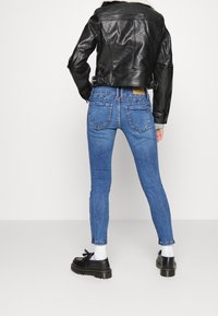 Chaqueta de cuero negra con cuello de borrego, llevada sobre unos vaqueros ajustados azules. Los vaqueros tienen bolsillos traseros y una ligera textura desgastada. Zapatos negros.