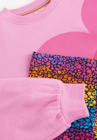 Felpa rosa con collo e polsini a costine, abbinata a tessuto fantasia che presenta disegni floreali multicolori e tonalità vivaci.