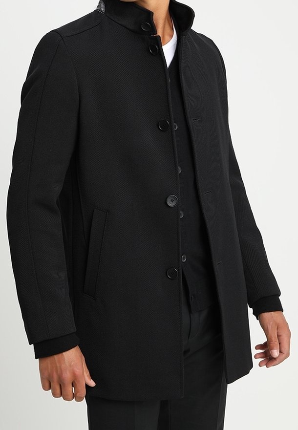 Cappotto nero in tessuto strutturato, colletto alto e chiusura a bottoni. Presenta due tasche laterali e polsini a coste per un tocco di dettaglio.