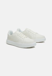 Weiße Leinensneaker mit glatter Textur, Gummisohle und flachen Schnürsenkeln. Sie verfügen über ein Low-Top-Design und minimale Details.