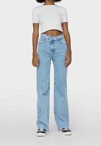 Jeans de tiro alto en azul claro con un corte relajado, presentan un diseño de pierna recta y un clásico diseño de cinco bolsillos, combinados con una blusa corta blanca.