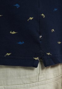 Námořnická polo košile s malými, vzorovanými rybičkami v modré a žluté. Vyrobena z texturované tkaniny s bočním rozparkem a šitým lemem.