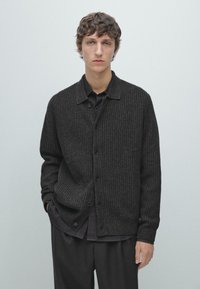 Dunkelgrauer, gerippter Strickcardigan mit Knopfleiste, klassischem Kragen und Seitentaschen, über einem schwarzen Hemd getragen. Die Textur ist weich und gemütlich.