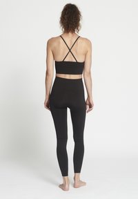 Top sportivo nero a manica corta con bretelle incrociate e leggings a vita alta, entrambi realizzati in materiale elasticizzato, design aderente, texture liscia.