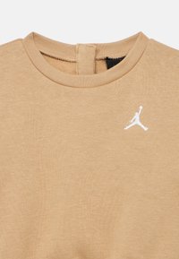 Μπεζ βαμβακερό μπλουζάκι με στρογγυλή λαιμόκοψη, μικρό λευκό λογότυπο "Jumpman" στο στήθος και ετικέτ α με θηλιά στο πίσω μέρος για εύκολη χρήση.