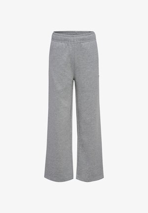 Dziecko o blond włosach do ramion, ubrane w granatową bluzkę z długim rękawem, szare szerokie spodnie i białe trampki, stojące na jednolitym tle.