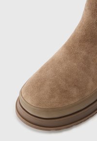 Braune Wildleder-Stiefelette mit abgerundetem Zehenbereich, strukturierter Oberfläche und einer dicken Gummisohle mit dezentem Rillenmuster.