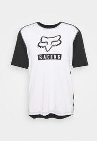 Tričko s krátkým rukávem, bílé barvy s černými rukávy. Na přední straně se nachází logo lišky a slovo "RACING" tučně napsané černými písmeny. Vyrobeno z hladké látky.