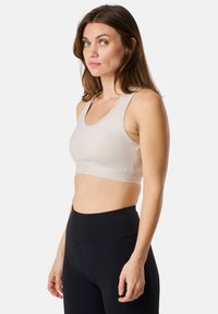 Soutien-gorge de sport beige avec un décolleté arrondi et des bretelles larges, équipé d'une bande inférieure texturée avec logo. Port�é avec un legging noir taille haute.