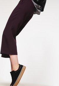 Burgundy capribyxor i slätt tyg med vida ben. Stylad med svarta mockaskor och diskreta nitar.