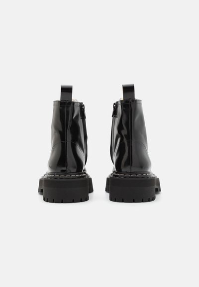 Schwarze Lackleder-Ankle Boots mit einer stabilen schwarzen Gummisohle, Reißverschluss und einem Ziehschlaufen auf der Rückseite. Glatte Oberfläche mit sichtbaren Nähten.