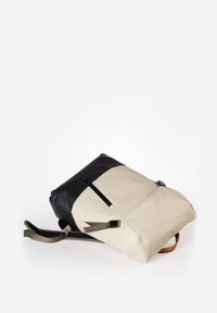 Rucksack mit einem cremefarbenen und schwarzen Farbblockdesign, hergestellt aus glattem synthetischem Material. Enthält verstellbare Träger und eine vordere Reißverschlusstasche.