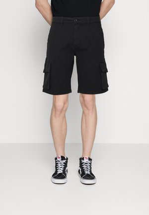 Pantalones cortos cargo negros de algodón, con bolsillos laterales y un corte regular. Combinados con zapatillas altas negras con cordones blancos.