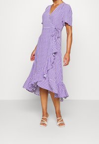 Vestito avvolgente viola con scollo a V, maniche corte e orlo arricciato. Presenta un motivo a quadri e un tessuto leggero.