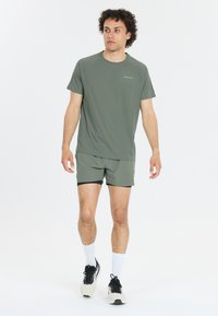 Korte mouwen, olijfgroen sportshirt met een aansluitend ontwerp. Gecombineerd met bijpassende shorts. Lichtgewicht, ademende stof met een subtiele logo.