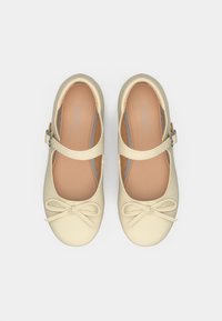 Παπούτσια στιλ Mary Jane σε απαλό μπεζ συνθετικό υλικό. Διαθέτουν λουράκι με ασημένια αγκράφα και λεπτομέρεια φιόγκου στο μπροστινό μέρος. Ομαλή υφή.