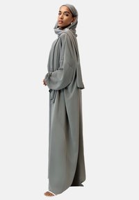 Abaya grise longue et fluide en tissu léger, dotée de manches longues et d'un hijab assorti. Design minimaliste, sans motifs ni accents.