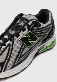 Chaussure de course grise et noire avec une tige en mesh, des accents vert lime et un logo distinctif. Semelle texturée avec plusieurs segments de amortissement.