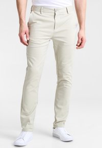 Chino beige chiaro realizzati in tessuto liscio, con vestibilità slim e tasche frontali, abbinati a sneakers bianche.