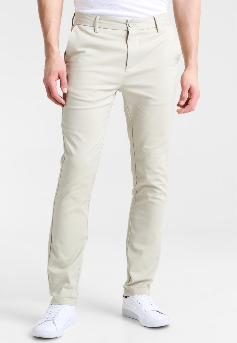 Chino beige chiaro realizzati in tessuto liscio, con vestibilità slim e tasche frontali, abbinati a sneakers bianche.