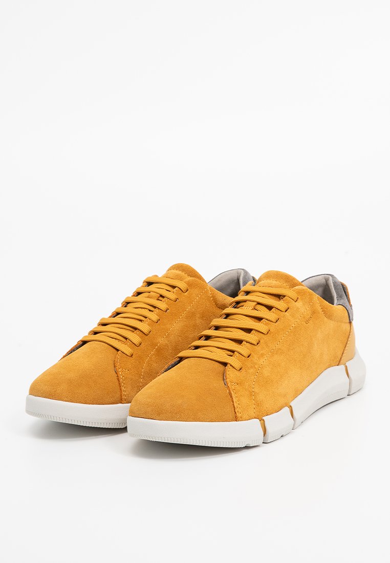 Żółte zamszowe trampki o teksturowanej powierzchni, z okrągłymi sznurówkami, białą gumową podeszwą i szarym akcentem na pięcie.